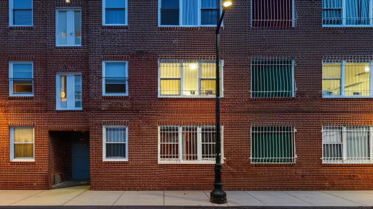 Exterior view of a ground-floor urban apartment building facade at dusk with barely visible interior window security bars