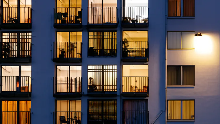 Ground-floor apartment building exterior at dusk showing interior window security bars silhouetted against warm interior lighting