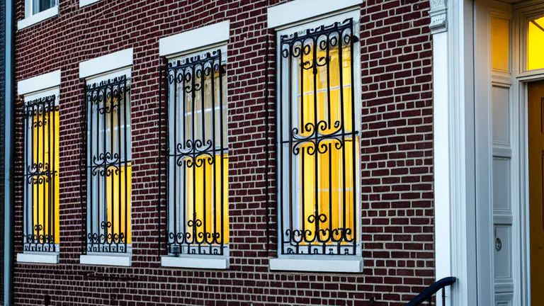 Historic brick rowhouse facade with ornamental scroll-work steel window security bars at dusk