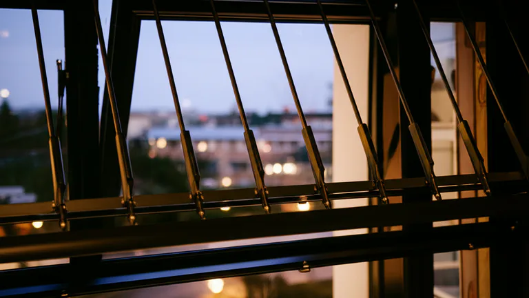 Telescopic window security bar installed without drilling on a ground-floor apartment window at dusk