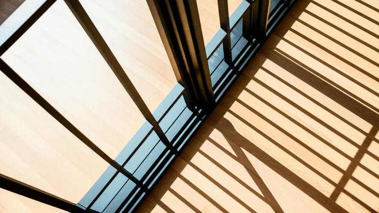 Overhead view of matte black steel window bars casting geometric shadow grid across hardwood interior floor, dramatic directional lighting